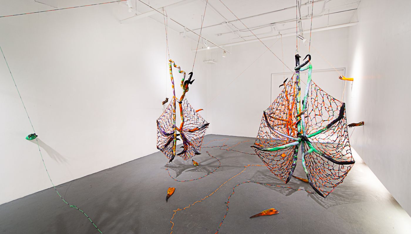 Installation of soft sculpture shaped in large bat-like wings where the membranes are knitted with beads, hands with nails on the wall pulling rope, and motorized tongues on the floor.