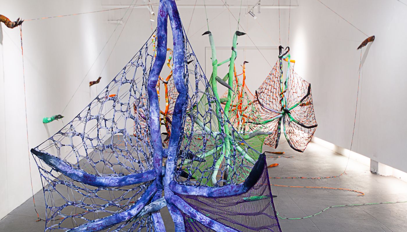 Installation of soft sculpture shaped in large bat-like wings where the membranes are knitted with beads, hands with nails on the wall pulling rope, and motorized tongues on the floor.