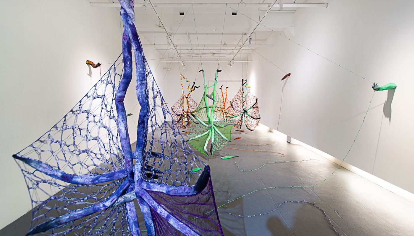 Installation of soft sculpture shaped in large bat-like wings where the membranes are knitted with beads, hands with nails on the wall pulling rope, and motorized tongues on the floor.