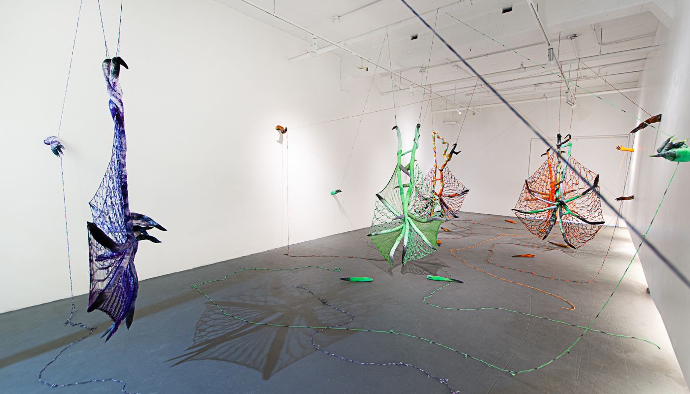 Installation of soft sculpture shaped in large bat-like wings where the membranes are knitted with beads, hands with nails on the wall pulling rope, and motorized tongues on the floor.