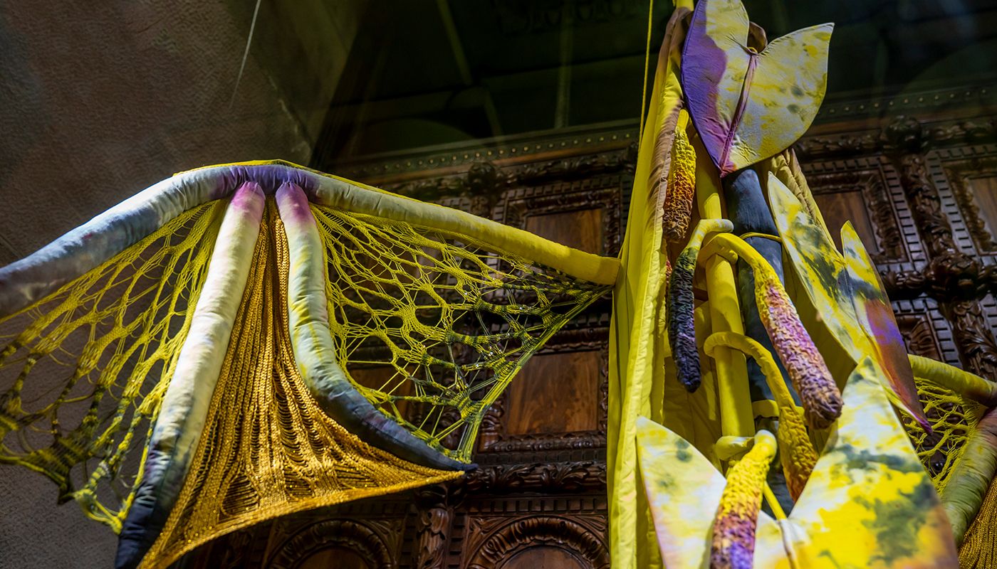 Installation of soft sculpture shaped primarily in yellow in large bat-like wings where the membranes are knitted with beads.