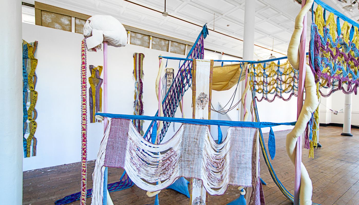 Colorful woven forms using backstrap weaving on fabric posts dyed with goldenrod, sappanwood, mulberry leaves, gardenia, annatto, logwood, and indigo.
