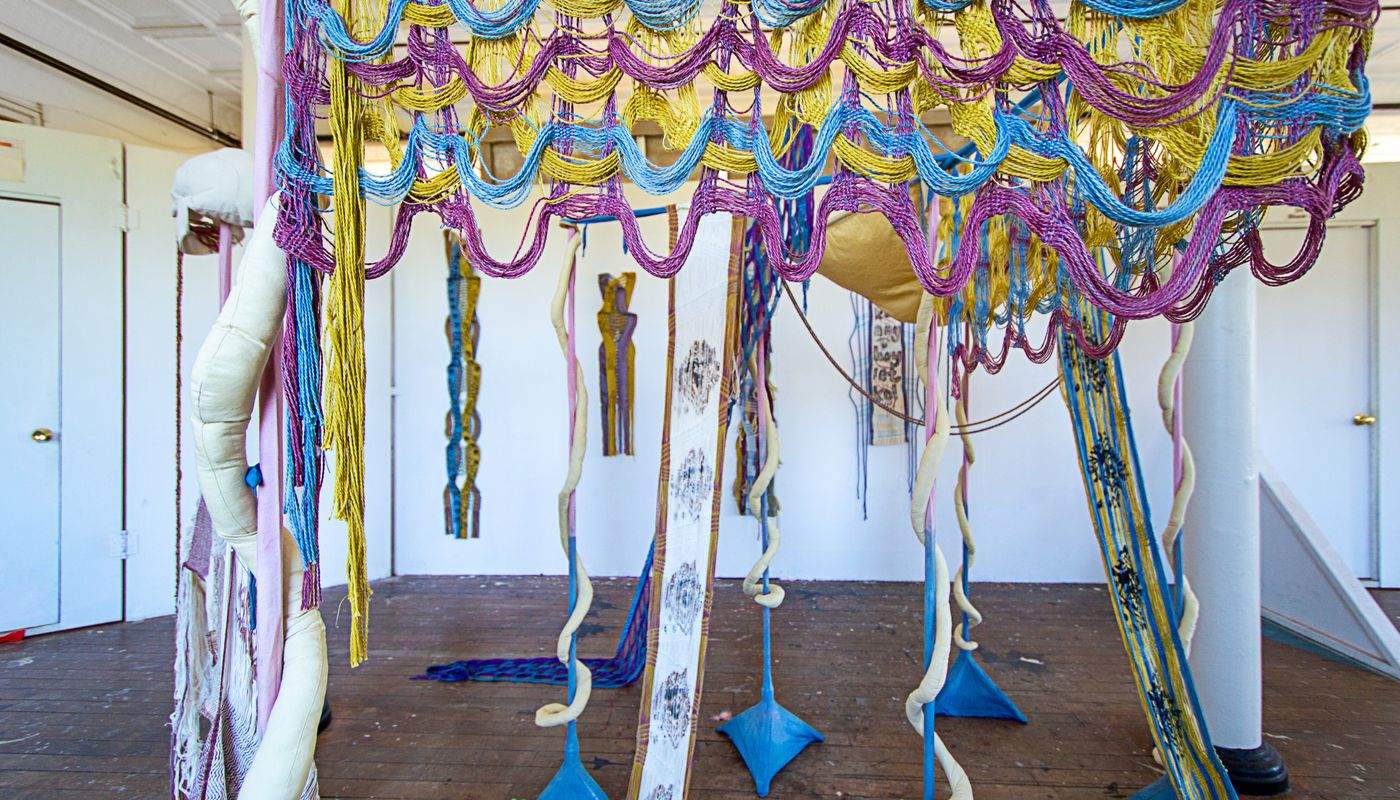 Colorful woven forms using backstrap weaving on fabric posts dyed with goldenrod, sappanwood, mulberry leaves, gardenia, annatto, logwood, and indigo.