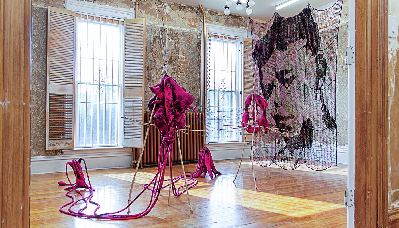 Installation of soft sculptures supported by bamboo structures extended with yarn to a large filet net with an embroidered portrait.