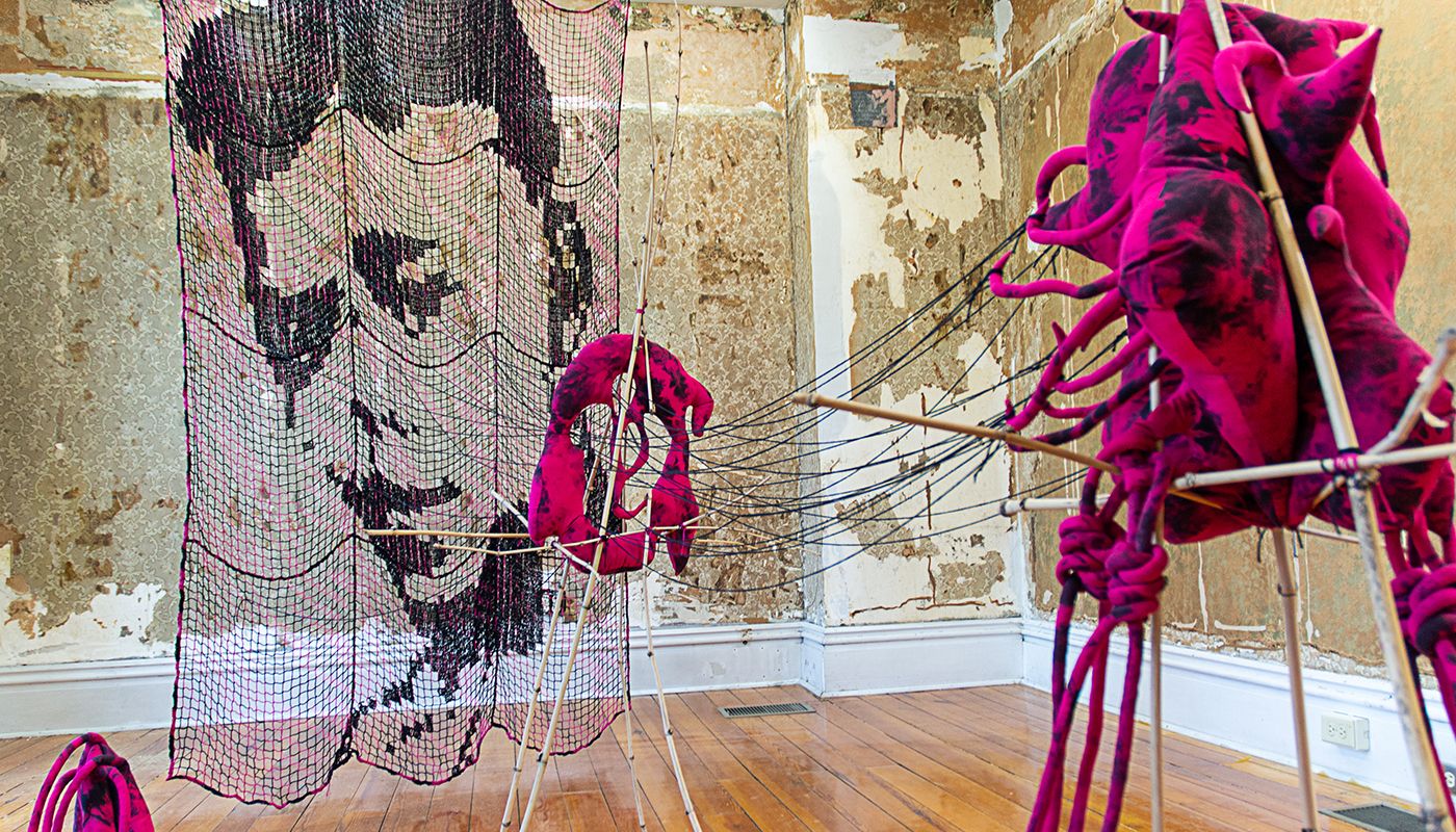 Installation of soft sculptures supported by bamboo structures extended with yarn to a large filet net with an embroidered portrait.