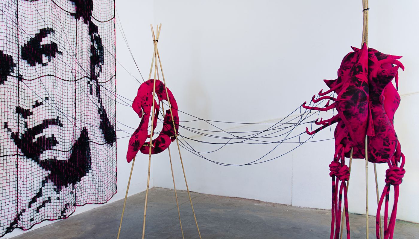 Installation of soft sculptures supported by bamboo structures extended with yarn to a large filet net with an embroidered portrait.