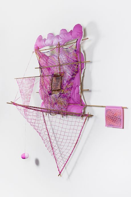 A wall soft sculpture tie dyed in hues of pink with filet lace and netting elements framed in bamboo that are tied using square lashing knots. Within the filet lace is an embedded gay pornographic image using a sublimation dye technique.