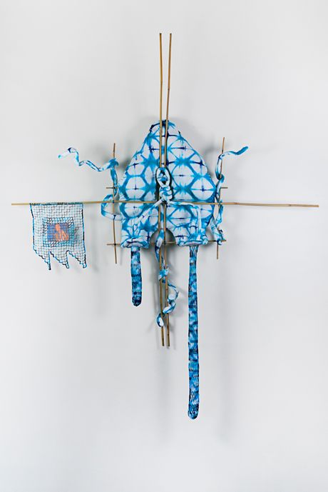 A wall soft sculpture tie-dyed in hues of blues with filet lace elements framed in bamboo that are tied using square lashing knots. Within the filet lace is an embedded gay pornographic image using a sublimation dye technique. 