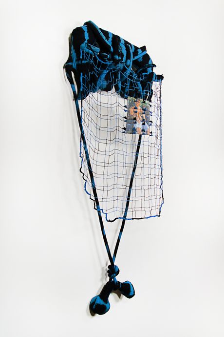 A wall soft sculpture tie dyed in black and blue with filet lace and netting elements. Within the filet lace is an embedded gay pornographic image using a sublimation dye technique.