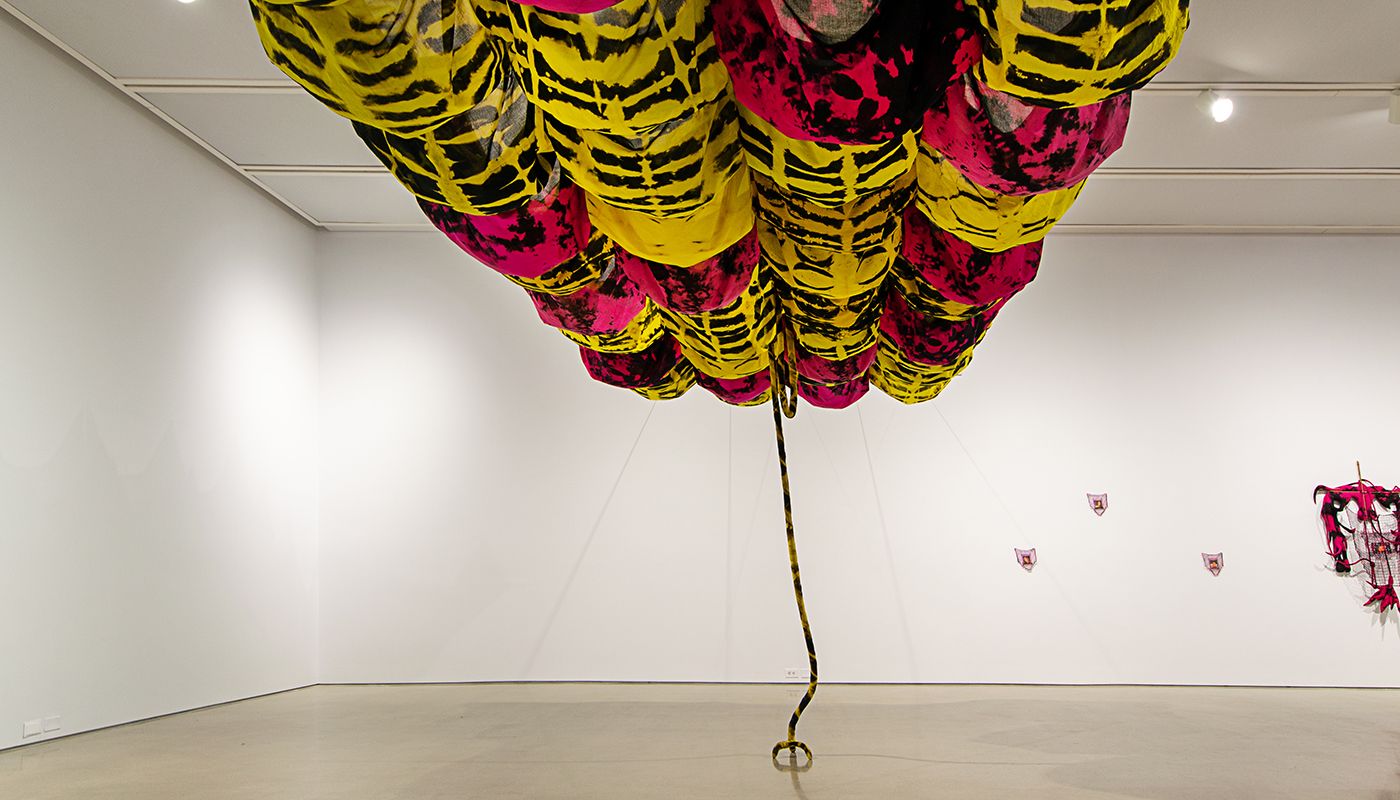 Free standing soft sculpture tie dyed in black and shades of pink and yellow supported in bamboo that are tied using square lashing knots with floating voile bulbous fabric and wall pieces.