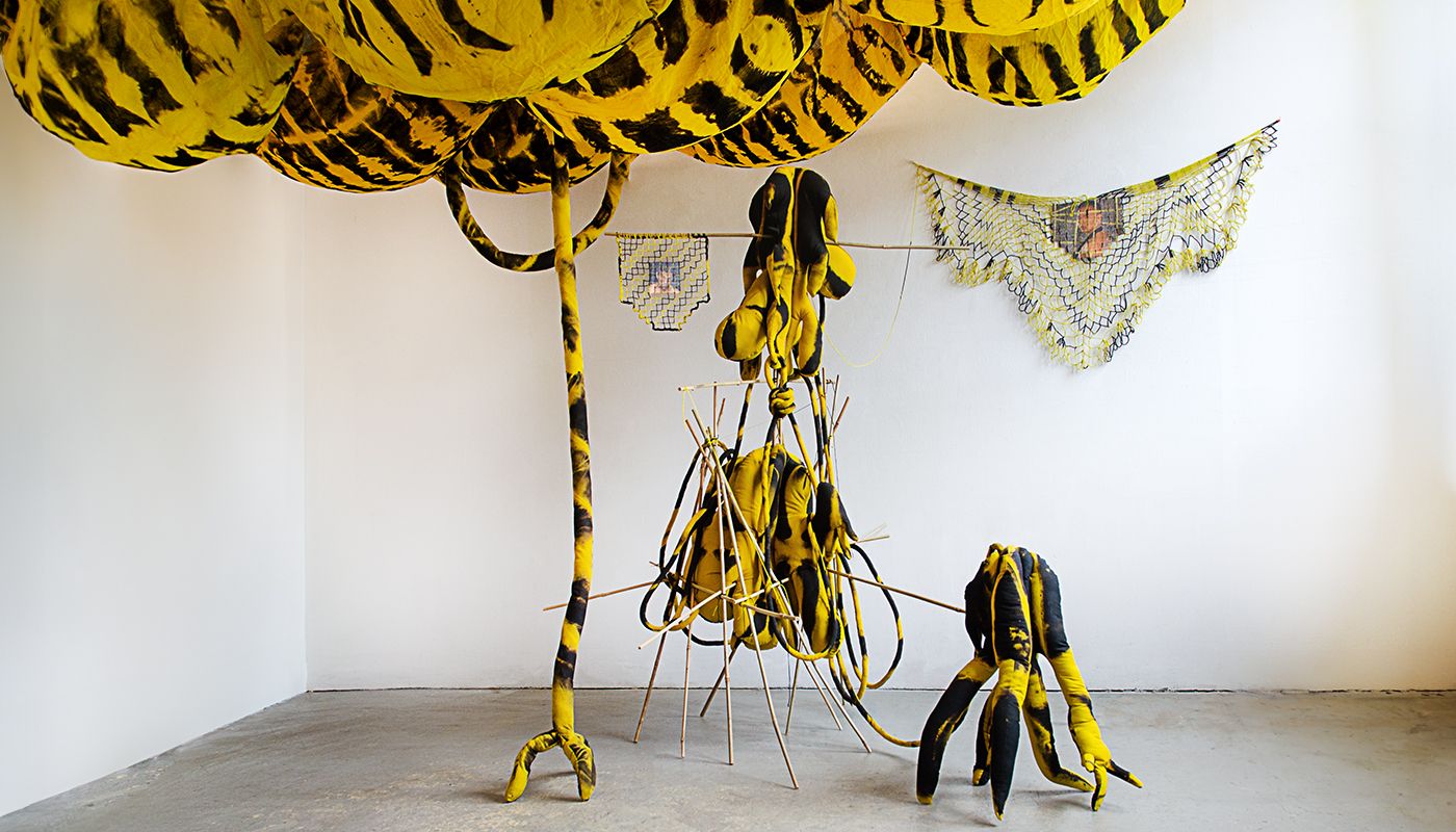 Installation of soft sculptures supported by bamboo structures with filet lace and bulbous voile fabric on the ceiling dyed in yellow and black.